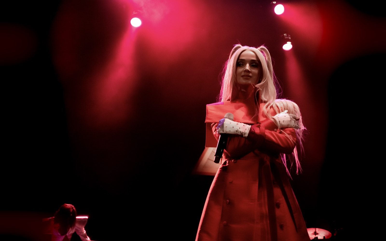 A wallpaper for Poppy: a concert photo of Poppy in a red coat under red stage lights, shown whole, its edges blending into a blurred extension of itself.